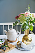 Blumenstrauß in goldener Vase auf gedecktem Tisch