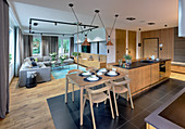 Küchentheke mit Barhockern und anschließendem Frühstückstisch, im Hintergrund elegante Lounge in offenem Wohnraum