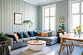 Graue Sofagarnitur, Couchtisch und Essbereich im Wohnzimmer mit hellgrün gestrichenen Holzwänden