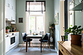 Table and two chairs below window in kitchen with houseplant on wooden table in foreground