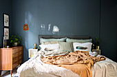 Double bed and retro chest of drawers in bedroom with grey-blue wall