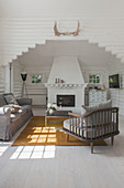 Sessel mit grauem Polster, passendes Sofa und Couchtisch vor Kamin in weiß gestrichenem Blockhaus