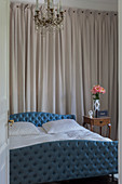 Bed with blue, button-tufted frame in bedroom with wall hanging