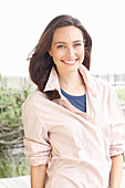 A young brunette woman wearing a blue t-shirt with a pale pink shirt blouse