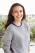 A young brunette woman wearing a grey woollen jumper with an under shirt