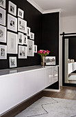 Gallery of pictures with white frames on black wall above sideboard