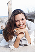 A young brunette woman wearing wearing a white tunic with a woollen jumper over her shoulders