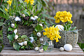 Moss wreath decorated with ivy berries, quail eggs, hay and feathers, Easter eggs, primrose and bouquet of daffodils