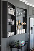 Crockery on grey wall-mounted shelves on grey wall above serving trolley