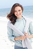 A young brunette woman wearing a light grey hooded top with a jumper around her shoulders