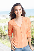 A young brunette woman wearing a salmon-pink tunic blouse
