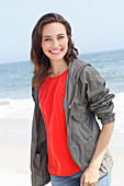 A young brunette woman wearing a red blouse, a grey windbreaker and jeans