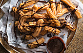 Pile of churros on spanish language newspaper drizzled with chocolate sauce