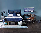 Double bed with blue headboard, next to desk with leather chair against blue wall