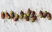 Flat-lay of chocolate glazed ice cream pops with pistachio icing over grey marble background