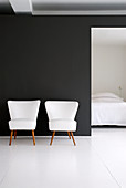 Zwei weiße Retro-Sessel vor schwarzer Wand, Blick ins Schlafzimmer
