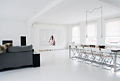 Grey sofa and long dining table in open-plan interior decorated entirely in white