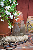 Ball of string, scissors and glass bottles in front of terracotta pots