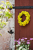 Gelber Blumenkranz an einer roten Scheunentür