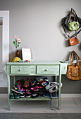 Stack of colourful sneakers on base of pale green console table against grey wall