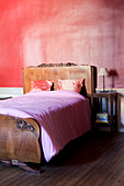 Antikes Holzbett mit Schnitzerei vor roter Wand im Schlafzimmer