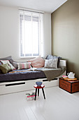 Vintage wooden trunk used as bedside table next to bed with collection of scatter cushions