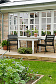 Black chairs at a table on a terrace in front of the brick house with lattice windows