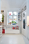 Chest bench under the window in the kitchen with white plank floor