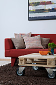 Pallet furniture on casters as a coffee table in front of the red sofa