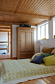 Bed with velvet scatter cushions in natural tones in rustic bedroom with wooden ceiling