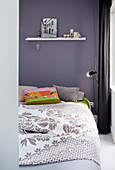 Double bed with bedspread and colourful scatter cushions against purple bedroom wall