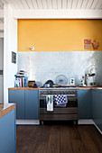 Wohnküche mit blau-grauen Unterschränken und gelber Wand