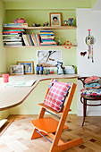 Children's chair at desk below shelves on green wall