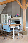 Farmhouse dining table with blue cantilever chairs in front of the fireplace in the dining room with rustic wooden beams