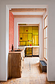 Eingebauter Massivholzschrank im Durchgang, im Hintergrund Küche mit gelber Glaswand