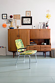 Chair in front of retro sideboard in living room with wooden floor