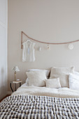 Queen size bed with pillows, ladies' blouse hanging on a wooden pearl garland in the bedroom in beige tones