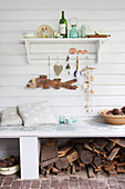 Maritime ornaments on shelf on board wall above bench with firewood stored below