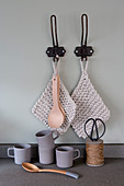 Knitted pot holders and wooden spoons hung from black hooks above mugs, spoon and reel of twine
