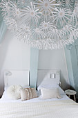 White double bed in the bedroom with light blue beams, in the foreground a romantic lamp