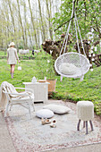 Idyllic garden space with hanging hammock chair, cushions, stool, and rattan armchair on carpet