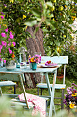 Gedeckter Tisch mit Blumen unterm Baum im sommerlichen Garten
