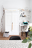 Weihnachtlich dekorierter weißer Schrank neben kleinem Schreibplatz und Ast mit Kugel-Lichterkette