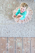 Soap bubbles above little girl wearing tutu and holding bead necklace on wool rug