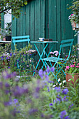 Türkisfarbene Gartenmöbel vor petrolblauer Bretterwand im blühenden Garten