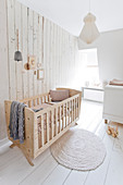 Crib in front of the wooden wall in the children's room all in white