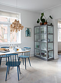 Blue sprouted chairs at the dining table in front of a glass cabinet with crockery