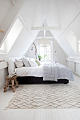 Rustic stool as a bedside table next to a double bed in the attic