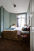 A double bed and a stool as a bedside table in a bedroom with a green wall