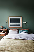 A picture above a double bed in a bedroom with a green wall